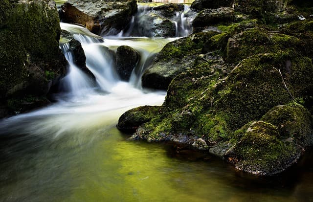 A stream falling over mossy boulders in woodland