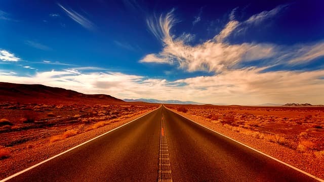 An empty desert highway running to the horizon under a blue sky
