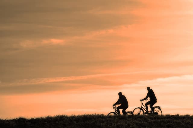 Two cyclists silhouetted on a ridge against an orange sky