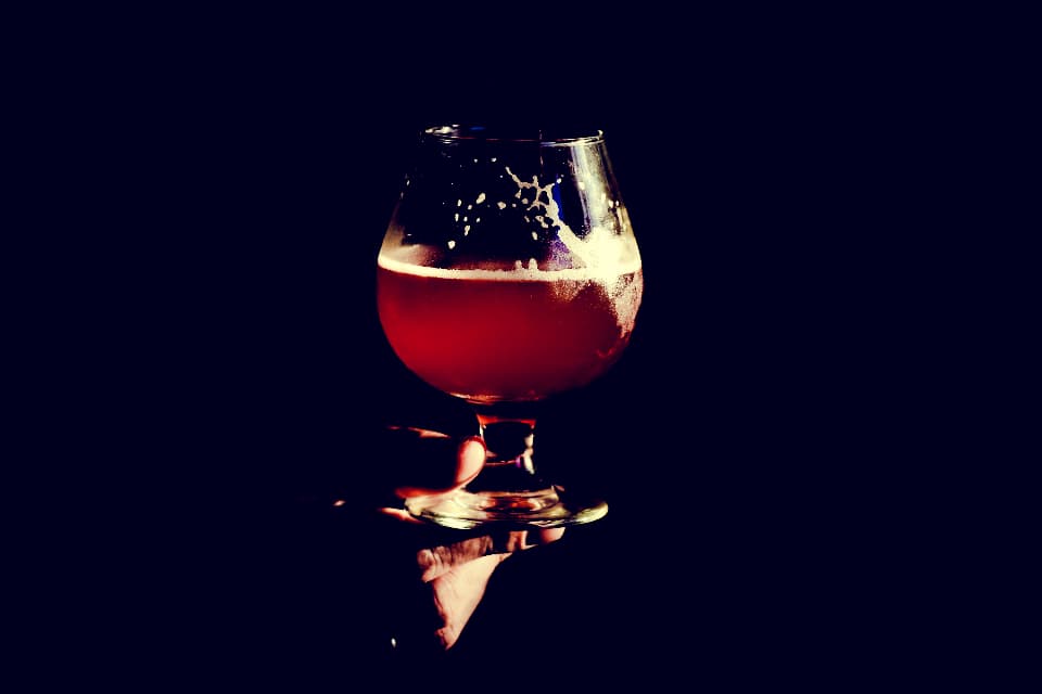 A snifter glass of amber beer lit against a dark background