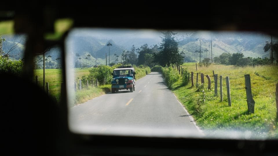 A jeep on a country road between green hills, seen through a vehicle windscreen