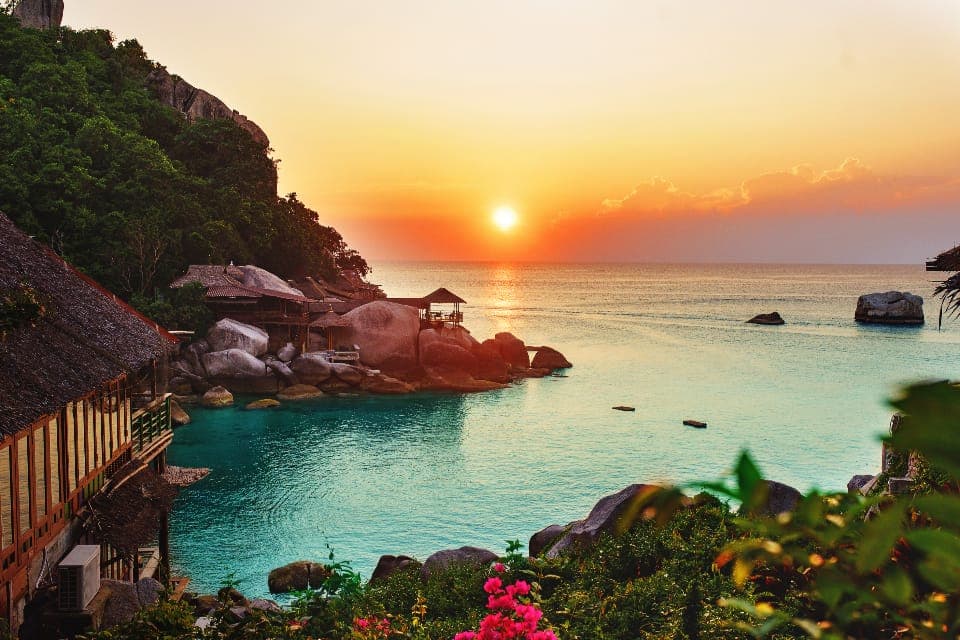 A tropical bay at sunset with a thatched roof above turquoise water