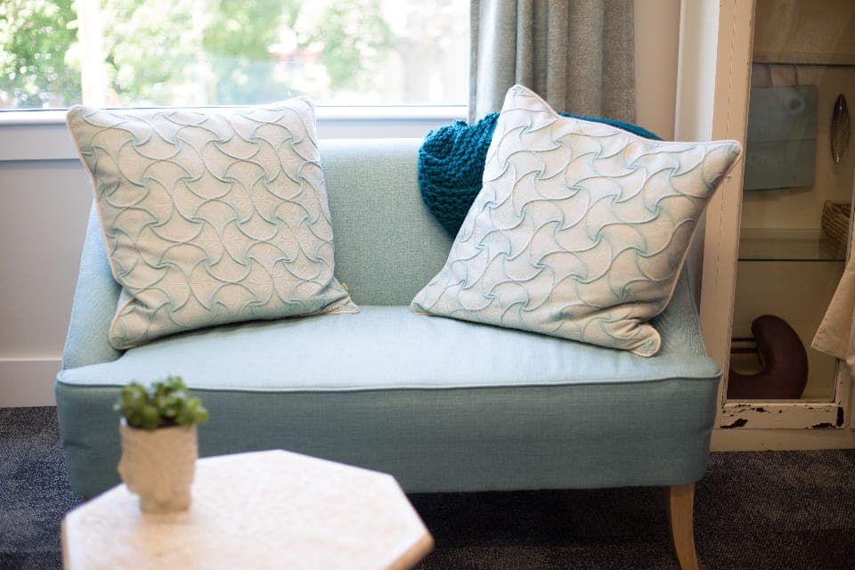 A pale blue loveseat with patterned cushions beside a window