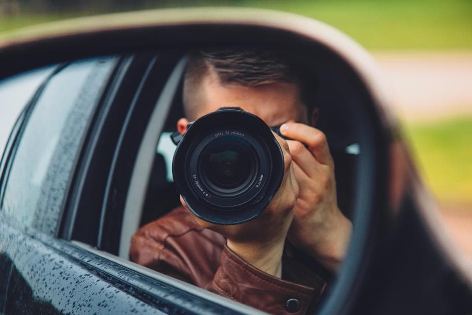 A photographer with a long lens reflected in a car wing mirror