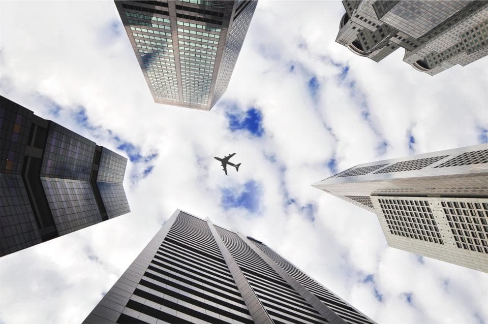 An airliner passing overhead, framed by glass office towers