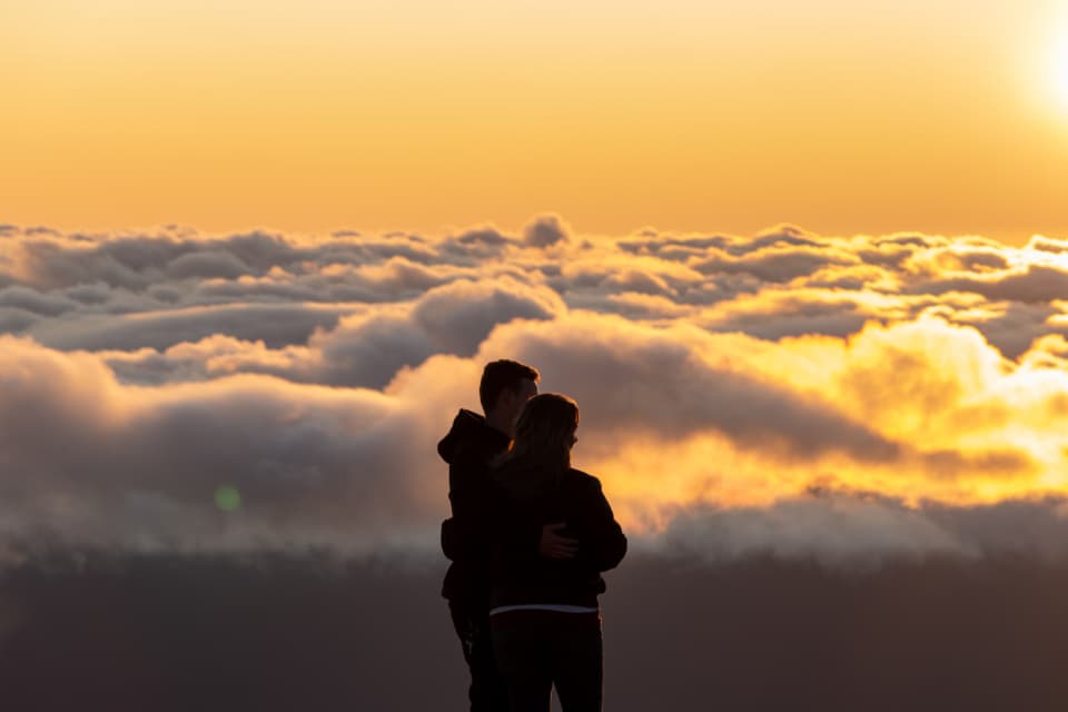 A couple silhouetted against a sea of cloud at sunset