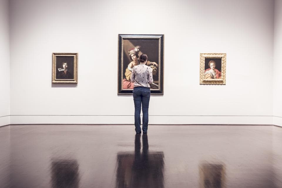 A visitor looking at framed paintings on a gallery wall