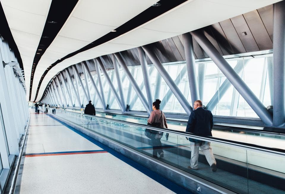 Travellers on a moving walkway in a glass airport corridor